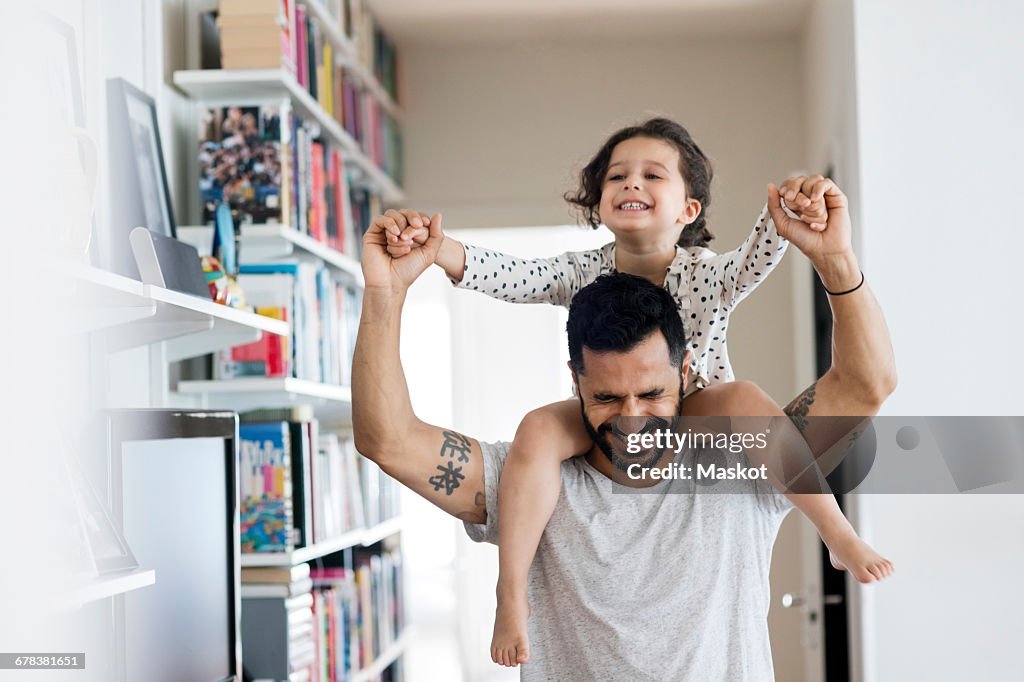 Happy father carrying girl on shoulder while standing at home