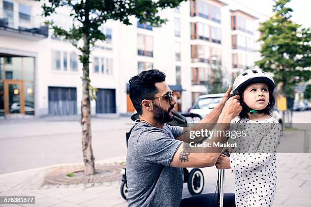 side view of father assisting daughter in wearing helmet at sidewalk - center street elementary - fotografias e filmes do acervo