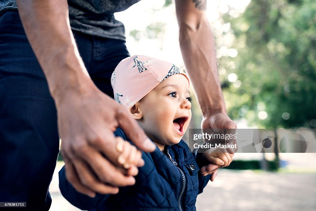 Midsection of father walking with toddler at park