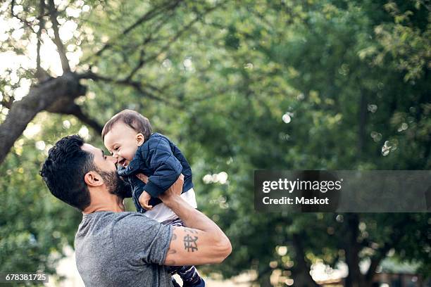 low angle view of smiling father picking up toddler at park - eltern baby hochheben stock-fotos und bilder