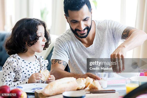 girl looking at smiling father pouring milk in glass during breakfast at home - two young arabic children only indoor portrait stock-fotos und bilder