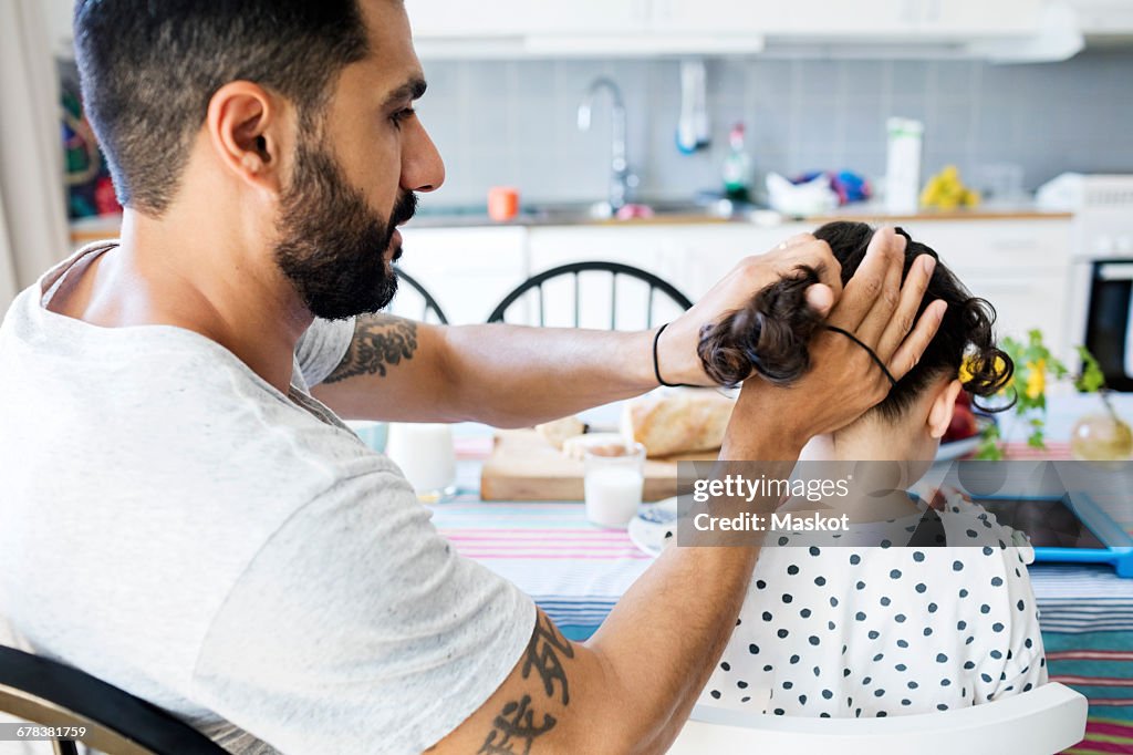 Father tying daughters hair while sitting at table