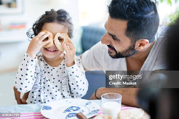 father looking at girl playing with bread slices during breakfast - two young arabic children only indoor portrait stock-fotos und bilder