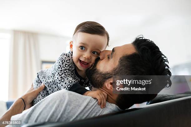 loving father kissing baby girl while sitting on sofa at home - lean in collection father stock pictures, royalty-free photos & images