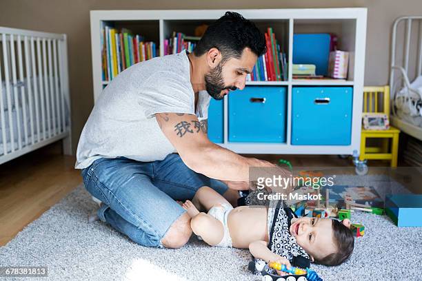 Father dressing up baby girl on carpet in bedroom