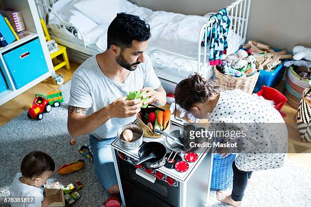 high angle view of father and children playing with toy kitchen in bedroom at home - kids mess carpet fotografías e imágenes de stock