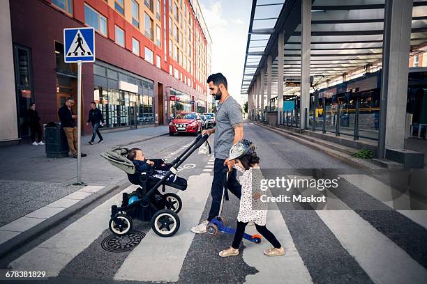 side view of father crossing street with daughter while holding baby stroller in city - paso de cebra fotografías e imágenes de stock