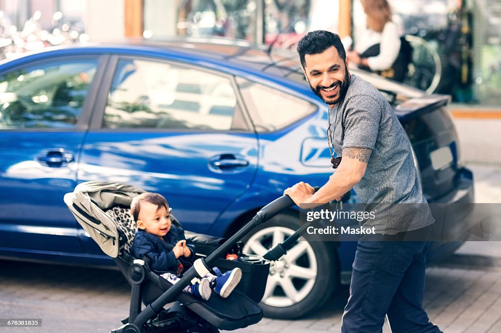 Father feeding toddler while standing by baby stroller on street