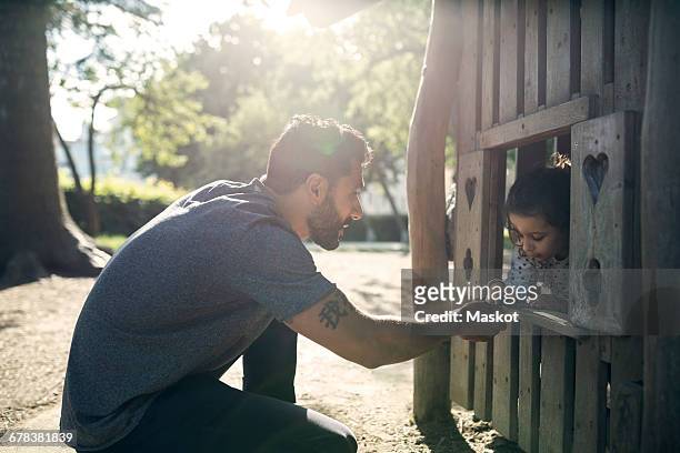 Side view of father and daughter playing in wooden toy house