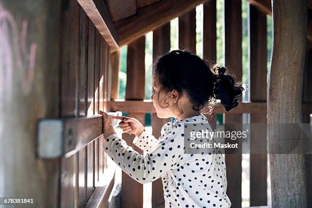 side view of smiling girl playing in wooden toy house - playhouse stockfoto's en -beelden