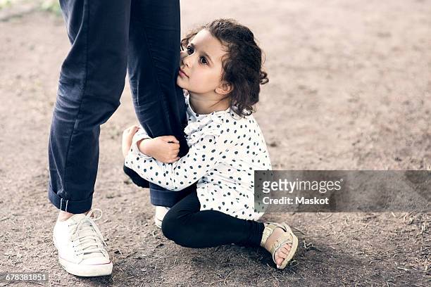 daughter gripping fathers leg while sitting on ground at park - gripping photos et images de collection