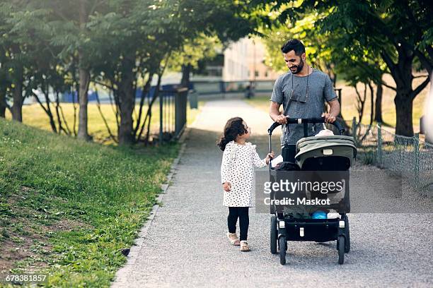 father and daughter talking while walking with baby stroller on footpath at park - lean in collection father stock-fotos und bilder