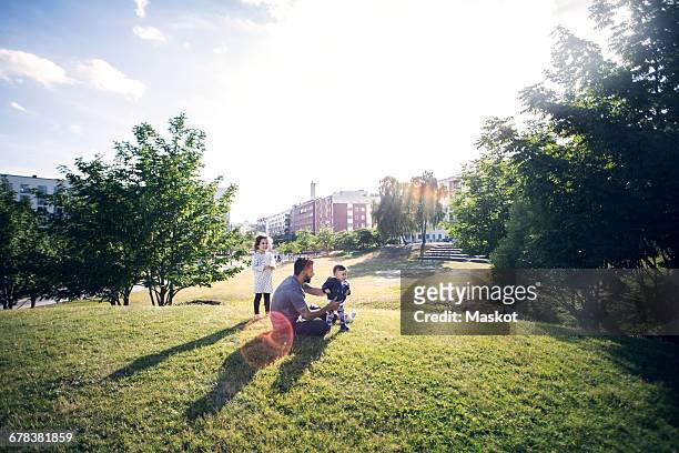 father playing with children on grassy field at park against sky - lifestyles photos et images de collection