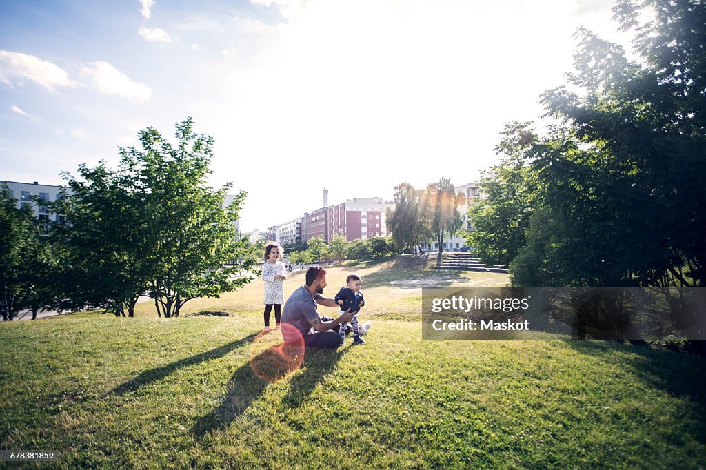 Father playing with children on grassy field at park against sky