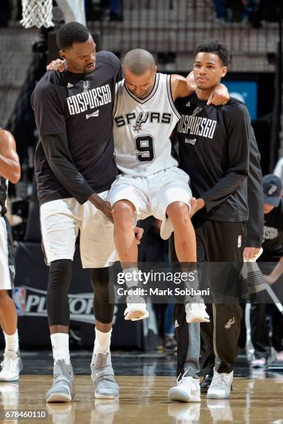 Dejounte Murray and Dewayne Dedmon carry Tony Parker of the San Antonio Spurs off the court after sustaining a knee injury during Game Two of the...