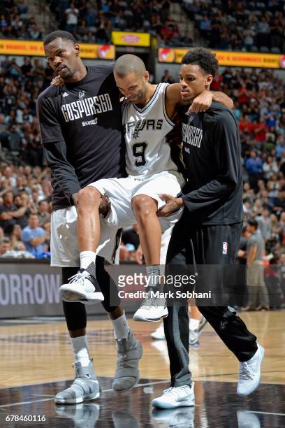 Dejounte Murray and Dewayne Dedmon carry Tony Parker of the San Antonio Spurs off the court after sustaining a knee injury during Game Two of the...
