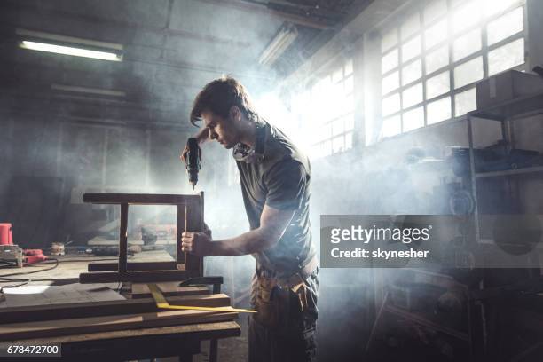 hombre carpintero utilizando taladro a una silla en un taller de reparación. - carpintero fotografías e imágenes de stock