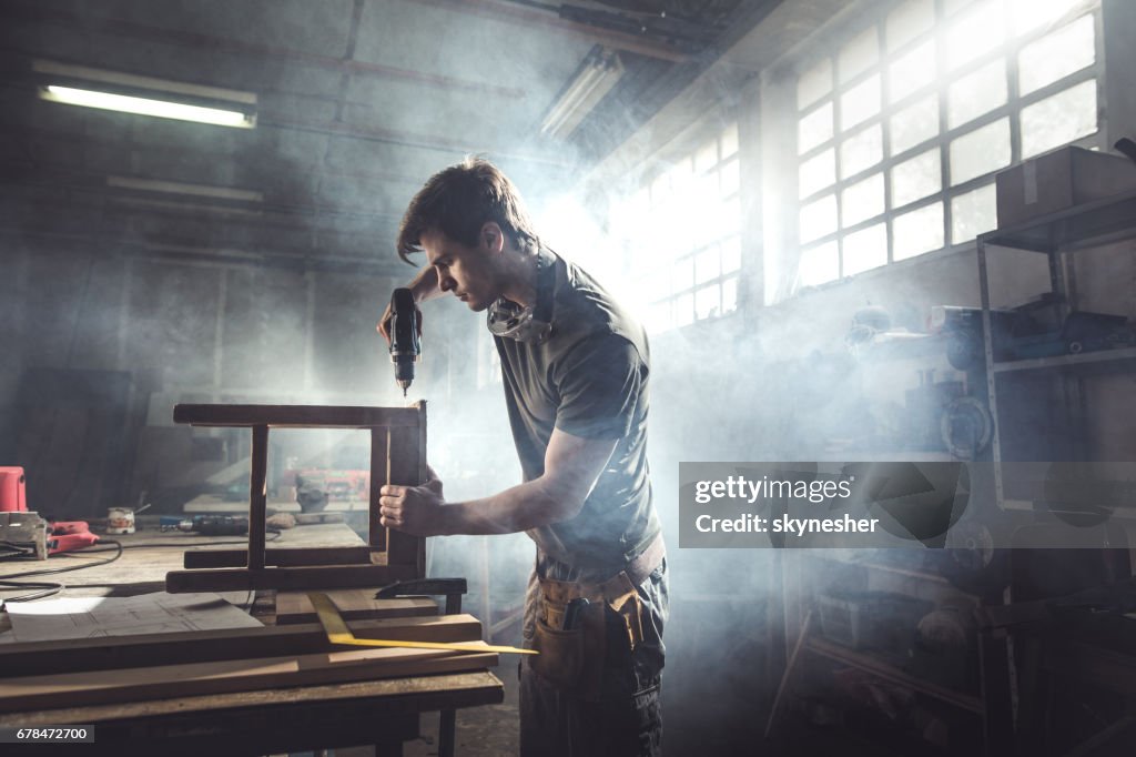 Male carpenter using drill to repair a chair in a workshop.