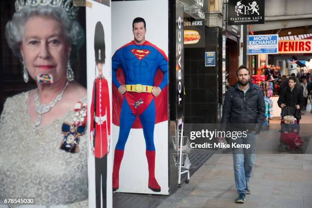 Queen Elizabeth II poster in a juxtaposition next to one of Superman and a member of the Guards wearing a bear skin at Leicester Square in London,...