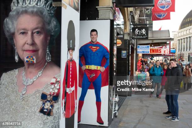 Queen Elizabeth II poster in a juxtaposition next to one of Superman and a member of the Guards wearing a bear skin at Leicester Square in London,...