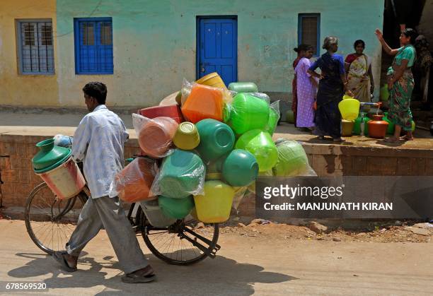 Vendor selling plastic pots on a bicycle walks past women collecting drinking water in plastic pots from a community tap in Bangalore on March 20,...