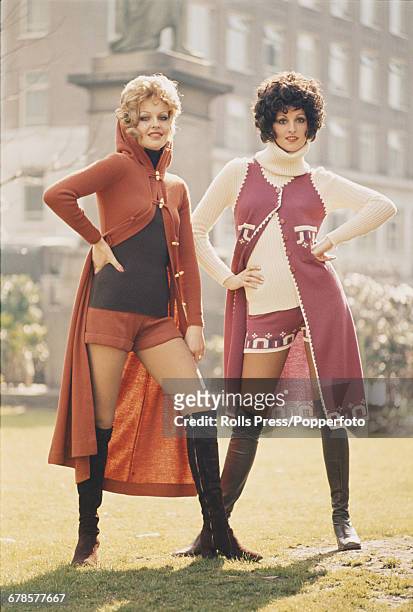 Seventies Fashion - model June Hodgson wears a long hooded duffel coat over hot pants and knee length suede boots next to fellow model Wendy Harman...
