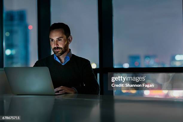 man viewing laptop computer in office at night - man using laptop fotografías e imágenes de stock