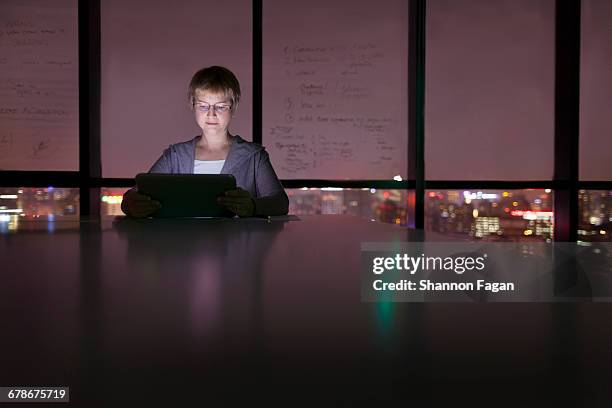 woman viewing tablet computer in office at night - the bigger picture stock pictures, royalty-free photos & images