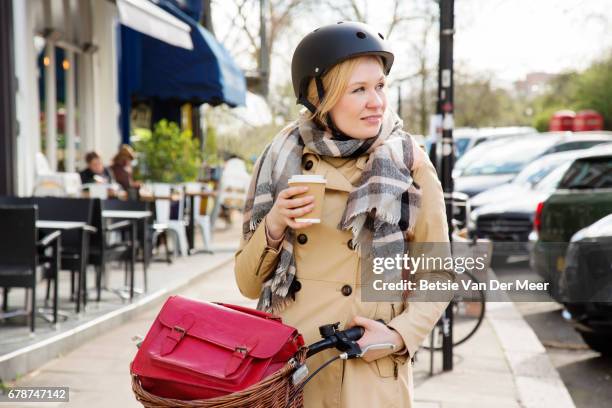 woman walks with coffee and bike in urban street on way to work. - bicycle basket stock pictures, royalty-free photos & images