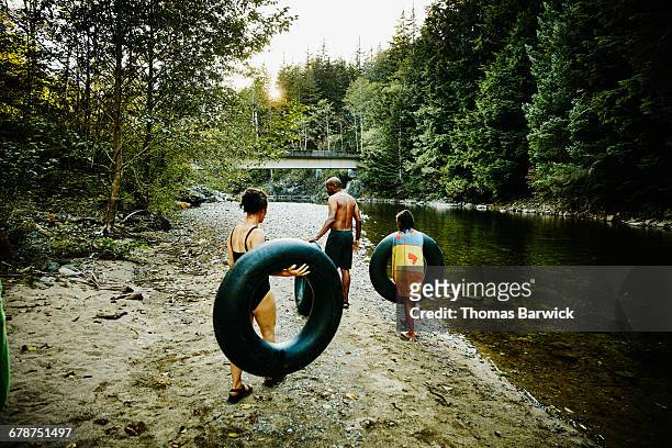 family walking next to river carrying inner tubes - river tubing stock pictures, royalty-free photos & images