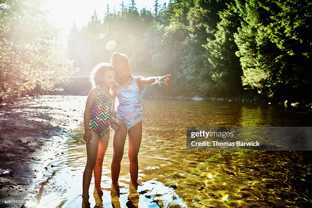 Sisters standing in river pointing upstream