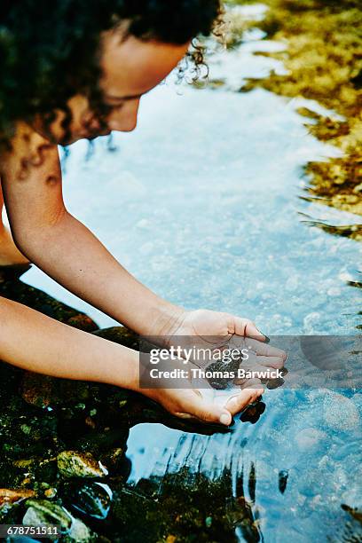 young girl looking at frog in her hands by river - frösche stock-fotos und bilder