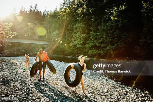 family carrying inner tubes by river - river tubing stock pictures, royalty-free photos & images