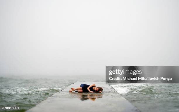 caucasian woman laying on dock in ocean waves - position du foetus photos et images de collection