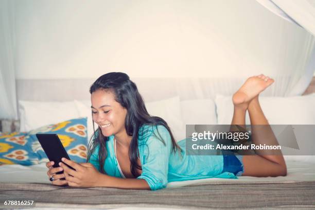 mixed race girl laying on bed reading digital tablet - girl bedroom stock pictures, royalty-free photos & images