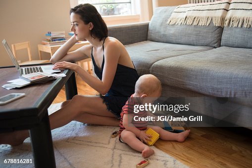Caucasian mother sitting on floor using laptop near baby son Caucasian mother sitting on floor using laptop near baby son