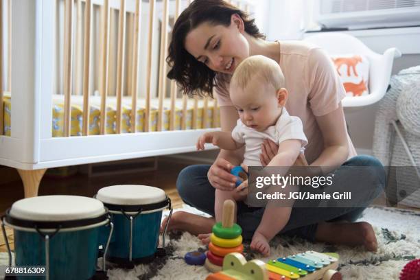 caucasian mother and baby son playing with toys on floor - mom sits on sons lap stock-fotos und bilder