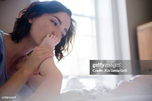 caucasian mother kissing foot of baby son on bed - foot kiss stock pictures, royalty-free photos & images