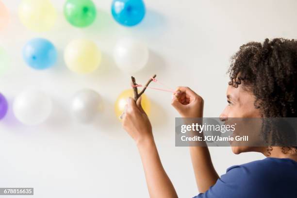 black woman aiming slingshot at balloons on wall - slingshot foto e immagini stock