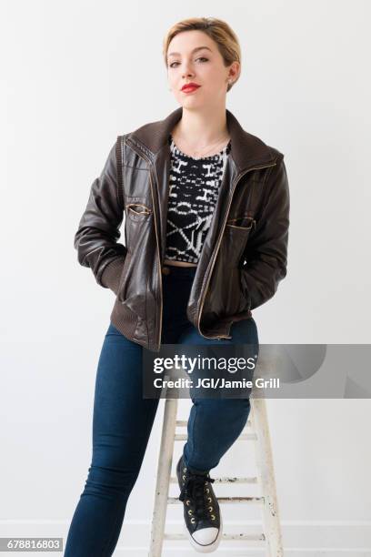 caucasian woman wearing leather jacket sitting on stool - woman stool stock pictures, royalty-free photos & images