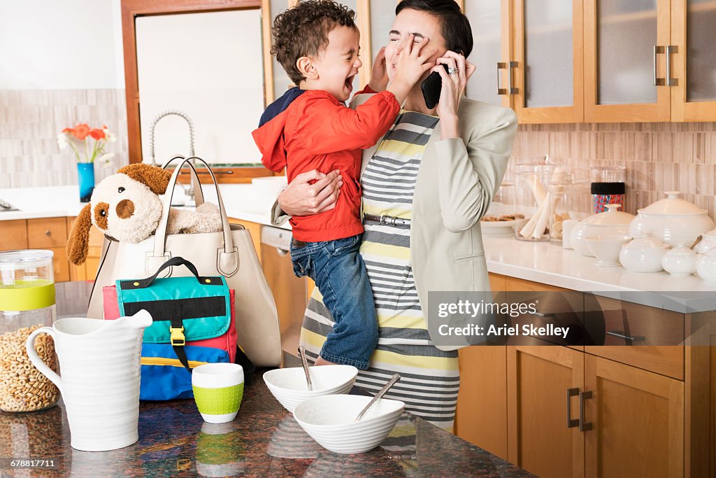 Mixed Race mother holding crying son while talking on cell phone