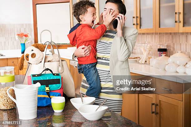 mixed race mother holding crying son while talking on cell phone - woedeaanval stockfoto's en -beelden