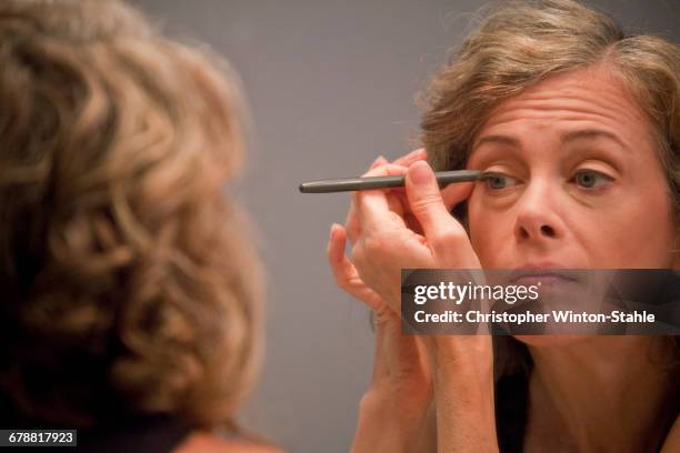 caucasian woman applying eyeliner in mirror - eyeliner stock pictures, royalty-free photos & images