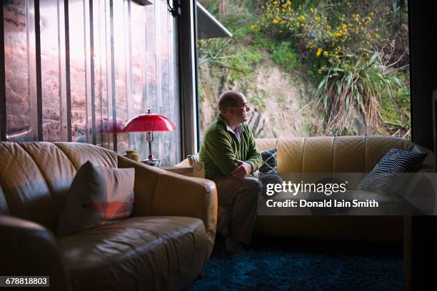 pensive caucasian man sitting on sofa near window - mann einsam stock-fotos und bilder