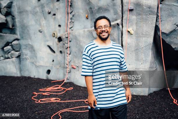Mixed Race man smiling near rock climbing wall