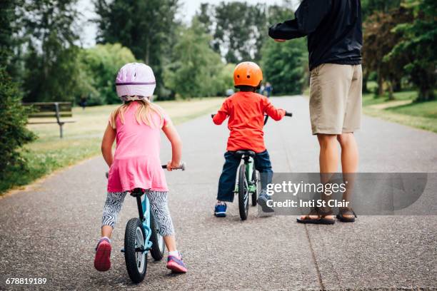 father watching daughter and son riding bicycles - lane sisters stockfoto's en -beelden