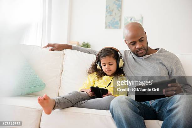 father and daughter using digital tablets on sofa - familie online stock pictures, royalty-free photos & images
