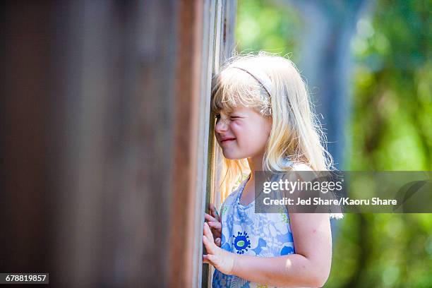 curious caucasian girl peeking through wooden fence - peephole stock-fotos und bilder