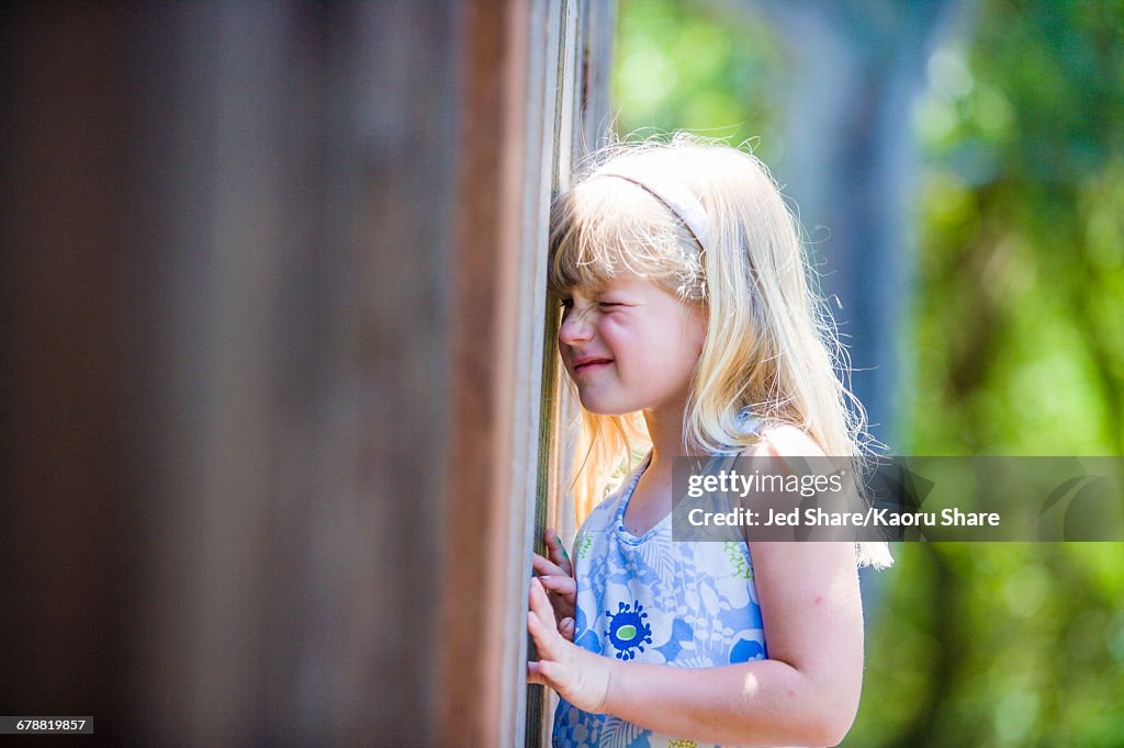 Curious Caucasian girl peeking through wooden fence