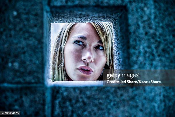 curious mixed race woman looking through stone wall - peephole stock pictures, royalty-free photos & images